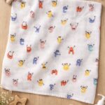 Soft white muslin baby swaddle towel with colorful alphabet character print laid flat on wooden surface