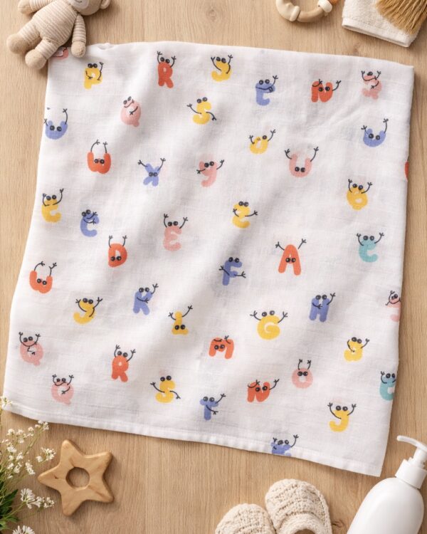 Soft white muslin baby swaddle towel with colorful alphabet character print laid flat on wooden surface
